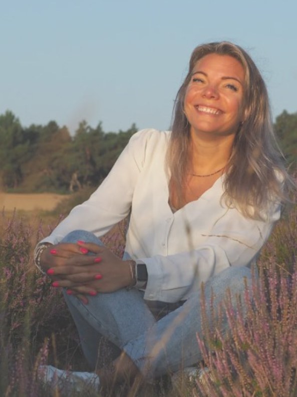 Bianca van Uden zit glimlachend in een veld met paarse heide