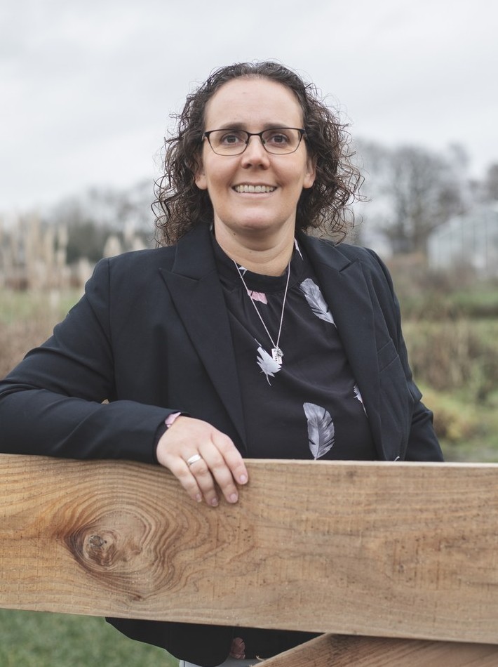 Femke Dirkx glimlacht buiten, met een veld op de achtergrond